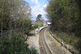 Single-track railway line running through woodland to a station with a curving platform
