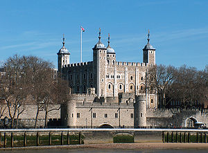 A keep seen from a river, rising behind a gate. The keep is large, square in plan, and has four corner towers, three square and one round, all topped by lead cupolas