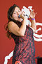 "A colour photo of Tagaq on stage singing. She is holding a microphone while wearing a red and black dress."